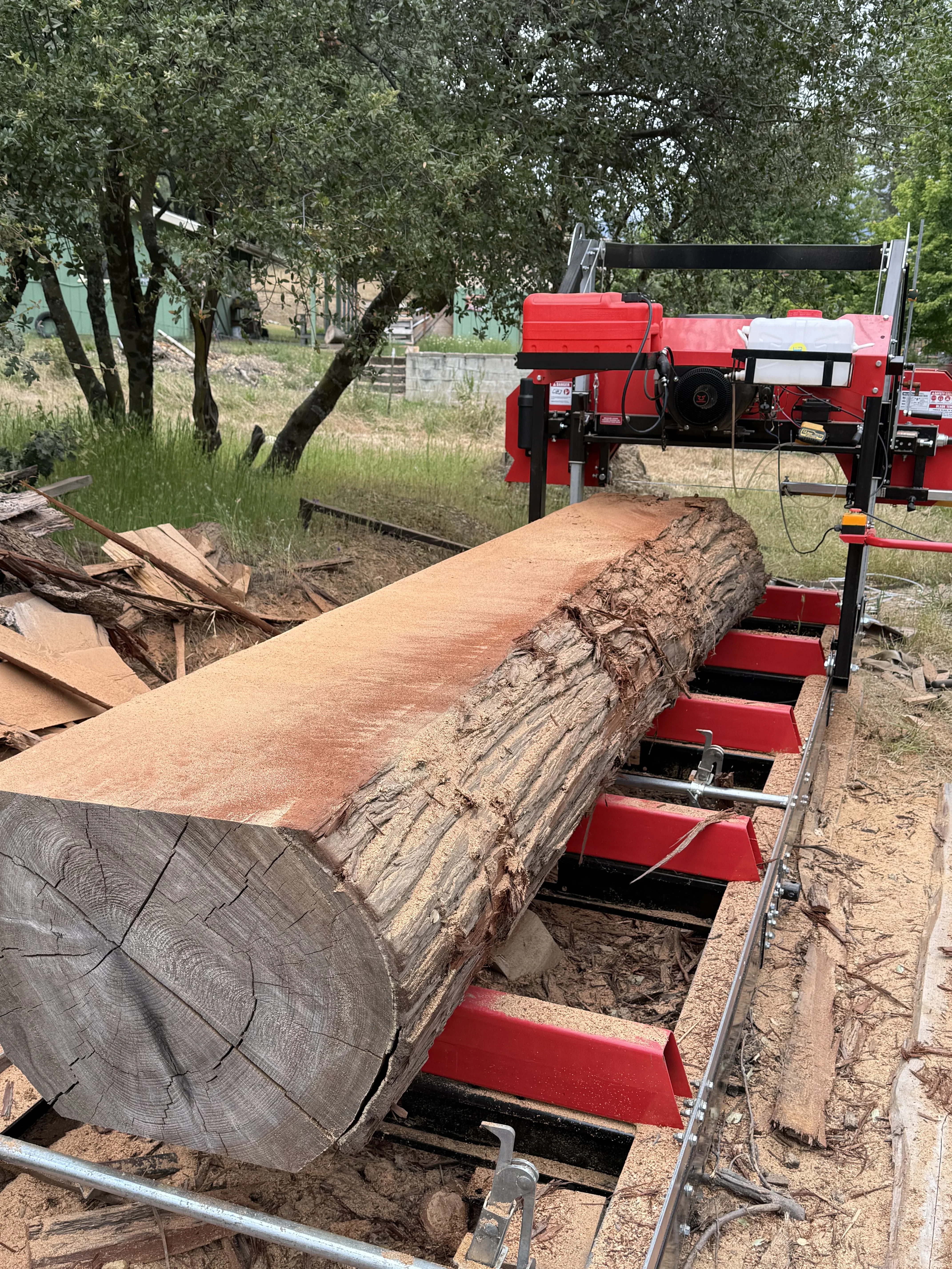 Portable sawmill processing large log with red hydraulic carriage and milled lumber sections