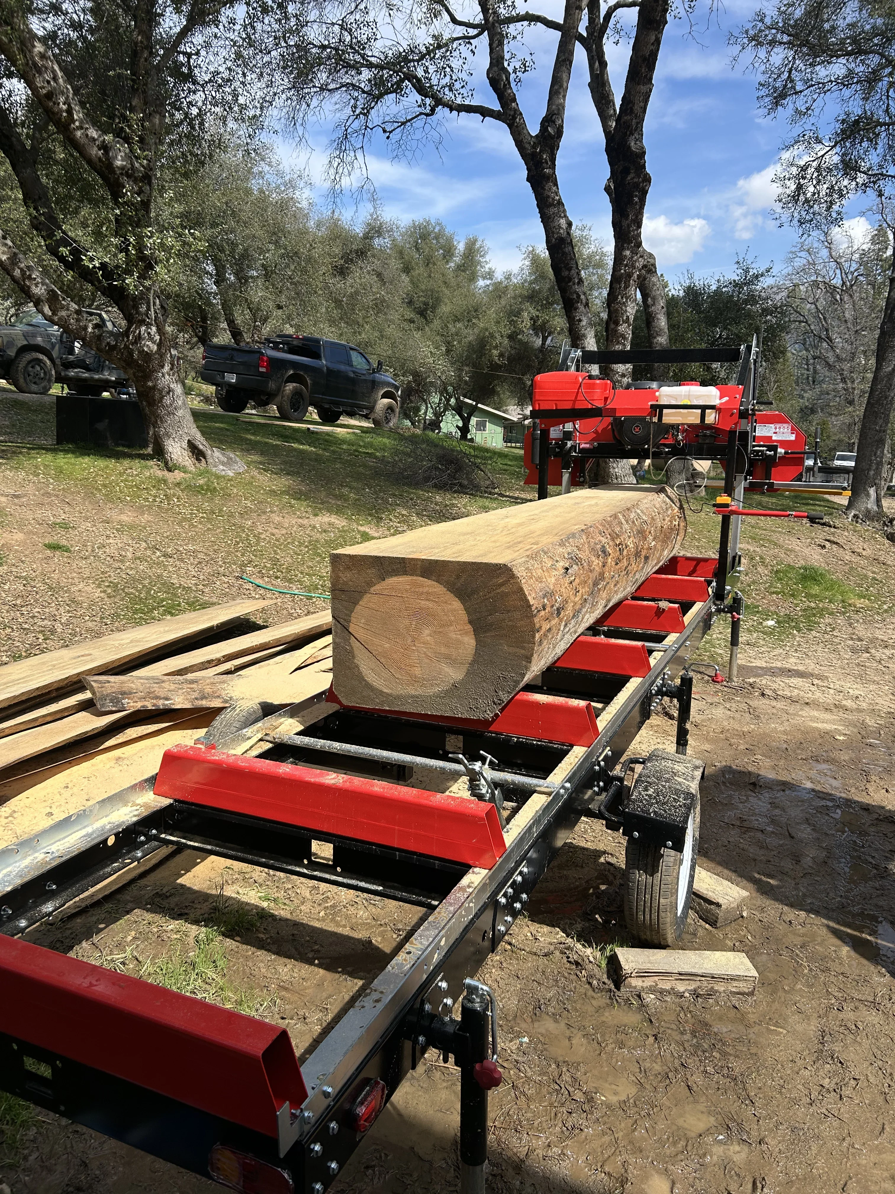 Large log on red portable sawmill with hydraulic conveyor system in wooded area