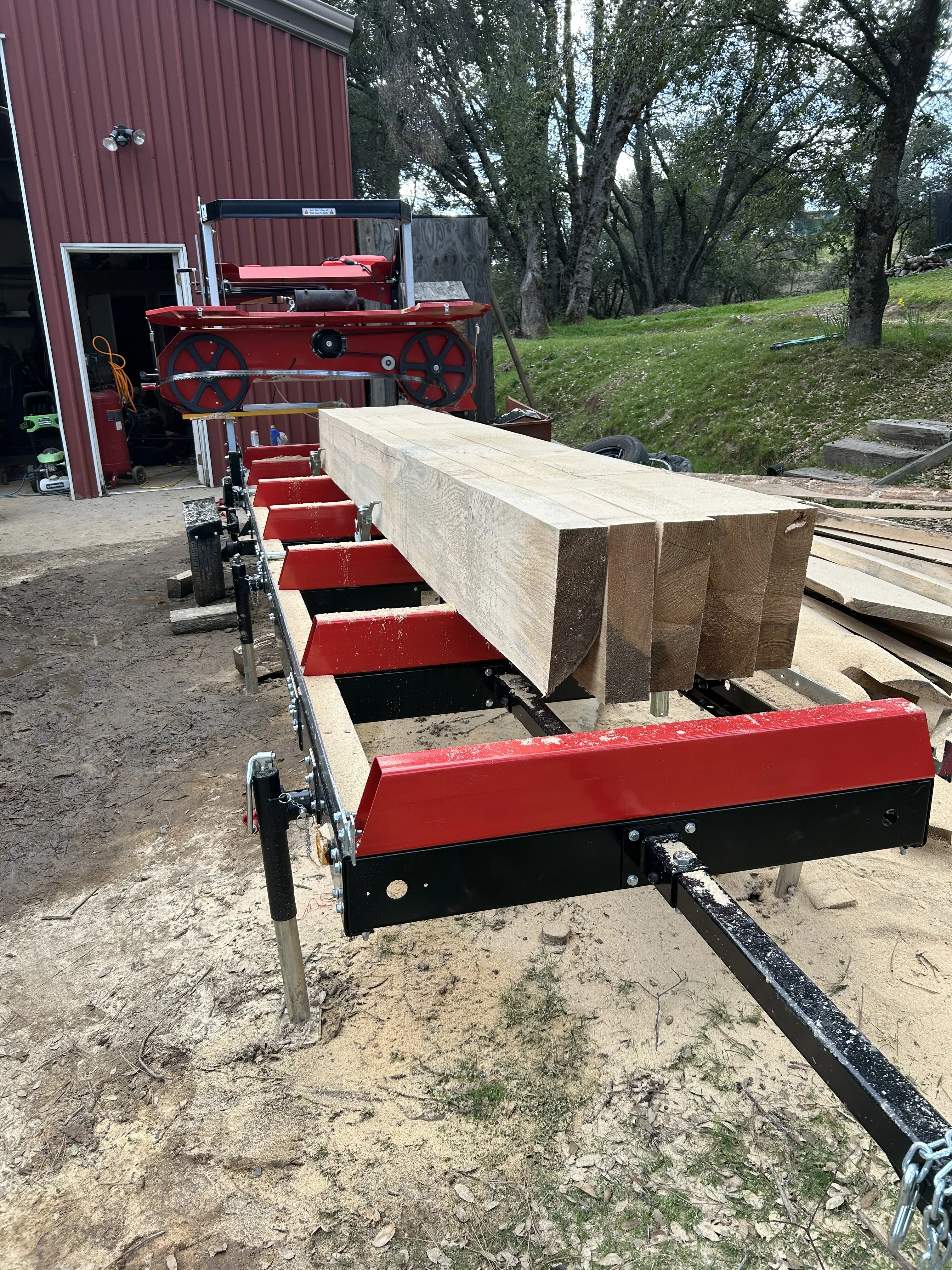 Portable sawmill processing large logs into lumber on red trailer system